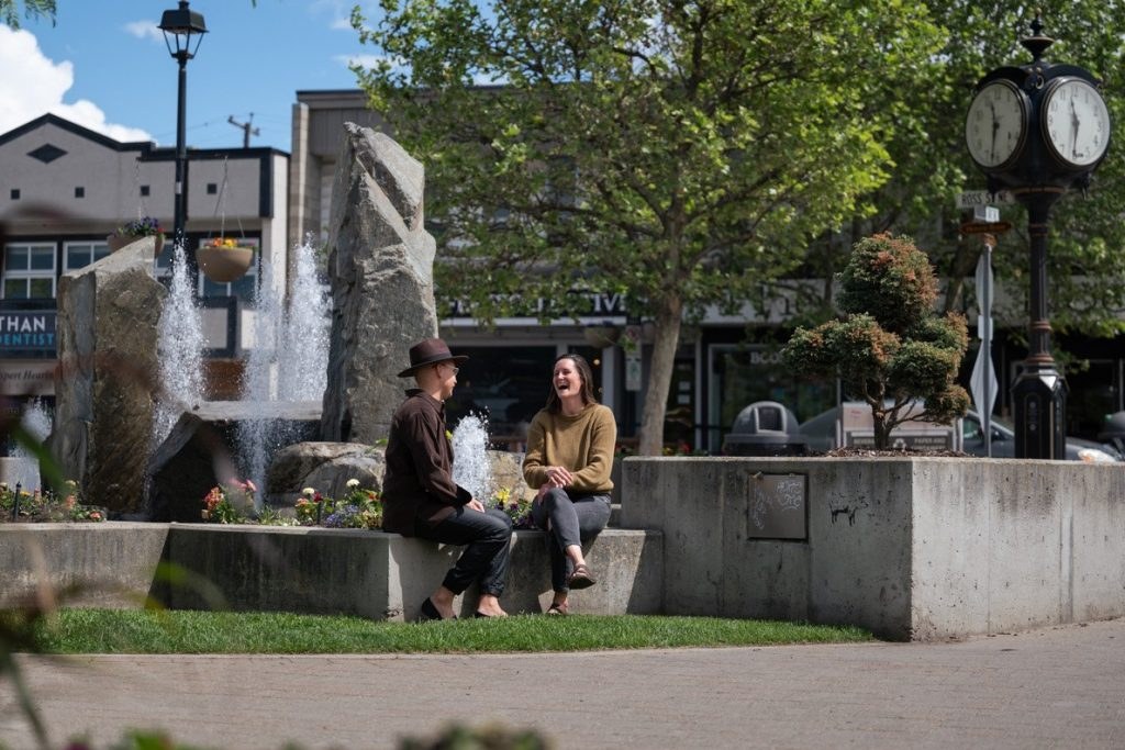 Two people laughing together by the fountain at Ross Street Plaza in downtown Salmon Arm
