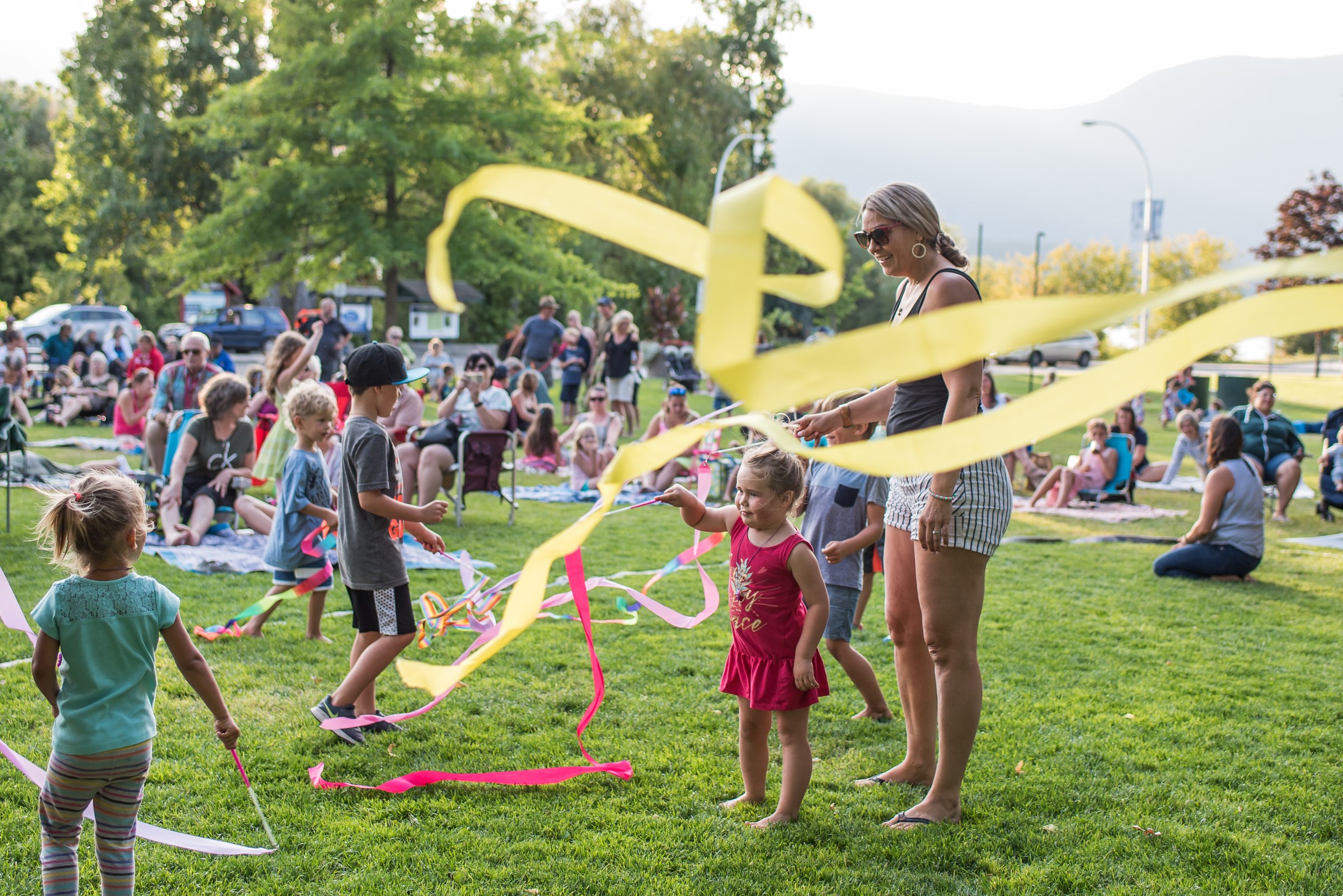 Children dancing with colourful ribbon streamers at an outdoor concert in the park