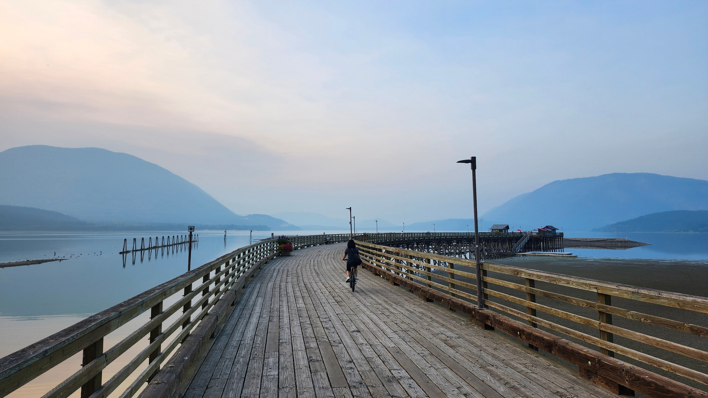 A cyclist riding the Marine Park wharf boardwalk at dusk over Shuswap Lake