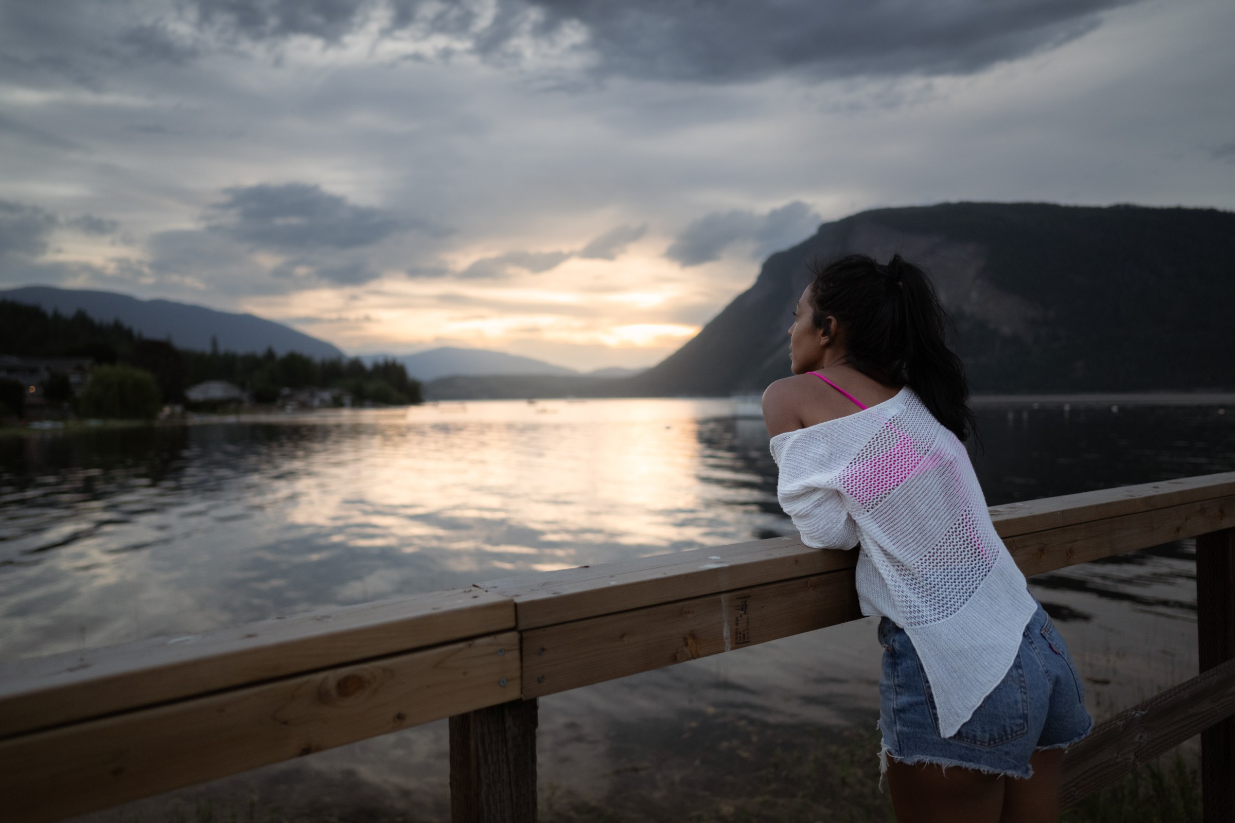 A woman leaning on the railing to take in a calm Shuswap Lake sunset