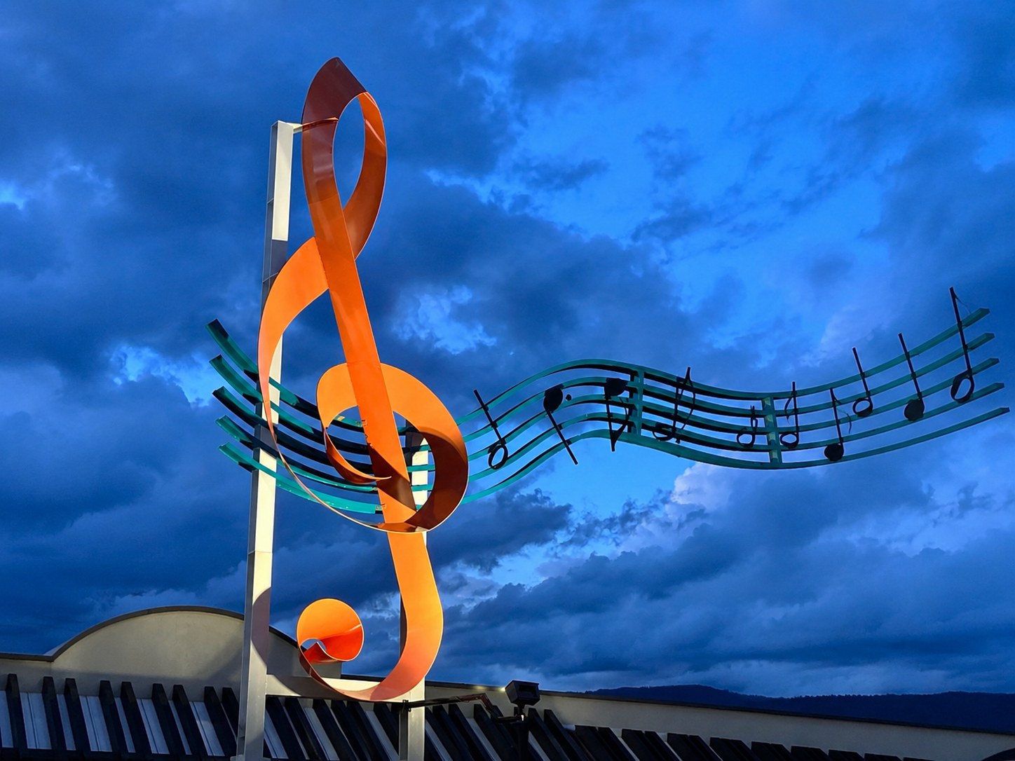 The World’s Largest Treble Clef — a giant orange treble-clef sculpture against a bright blue sky on Alexander Street